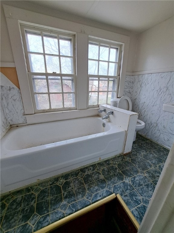 full bath with a garden tub, toilet, tile walls, wainscoting, and tile patterned floors