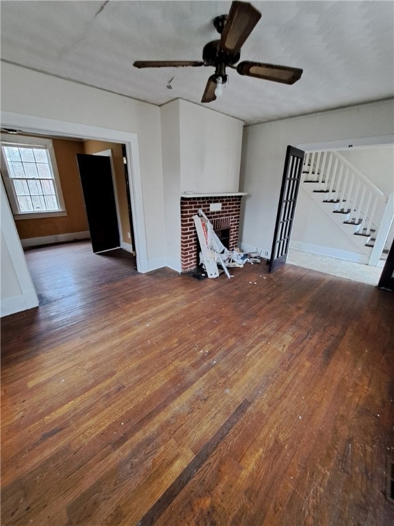 unfurnished living room with a fireplace, a ceiling fan, baseboards, stairway, and wood-type flooring