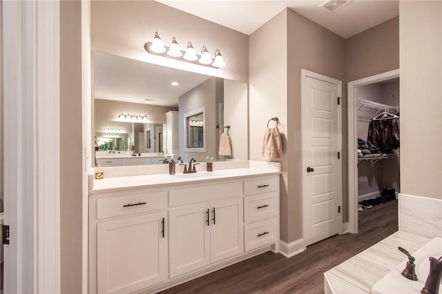 full bath featuring wood finished floors, visible vents, vanity, baseboards, and a spacious closet