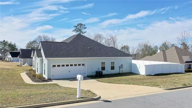 view of side of property featuring an attached garage, central air condition unit, fence, driveway, and a lawn