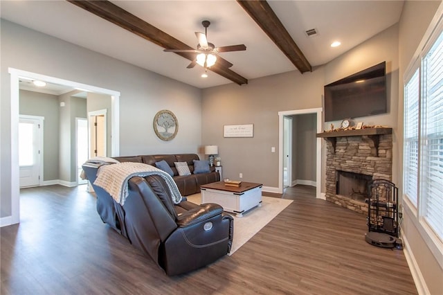 living room with visible vents, baseboards, dark wood-style flooring, a stone fireplace, and beam ceiling