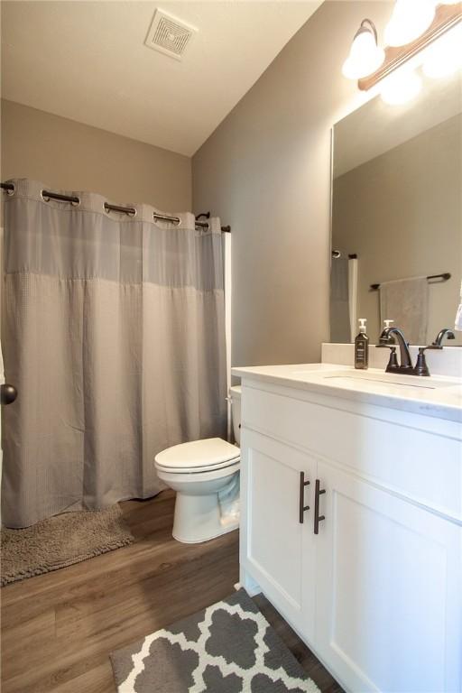 bathroom with visible vents, a shower with shower curtain, toilet, wood finished floors, and vanity