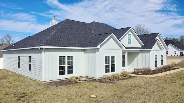 rear view of property featuring a chimney, board and batten siding, and a yard