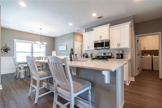 kitchen with a breakfast bar area, stainless steel appliances, visible vents, backsplash, and washer and clothes dryer