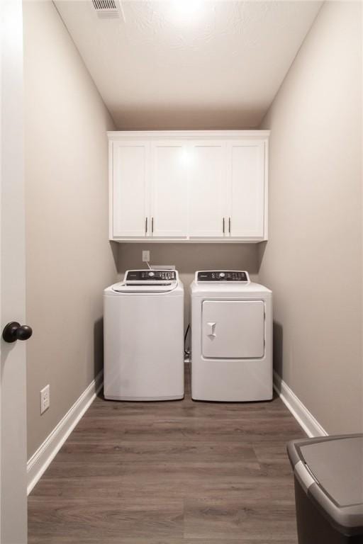 laundry room featuring wood finished floors, washing machine and dryer, cabinet space, and baseboards