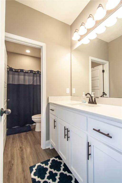 bathroom featuring wood finished floors, vanity, toilet, and curtained shower