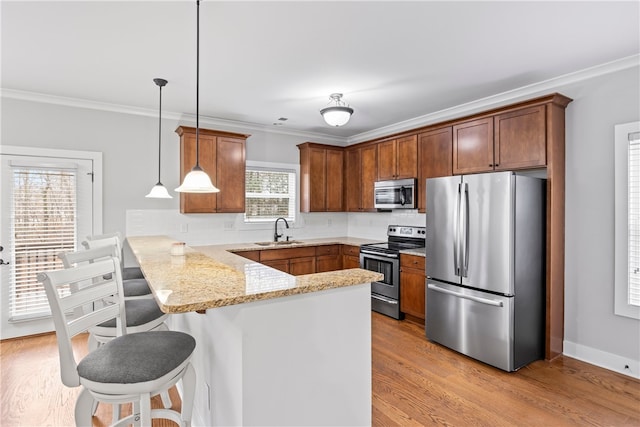 kitchen featuring sink, appliances with stainless steel finishes, hanging light fixtures, a kitchen bar, and kitchen peninsula