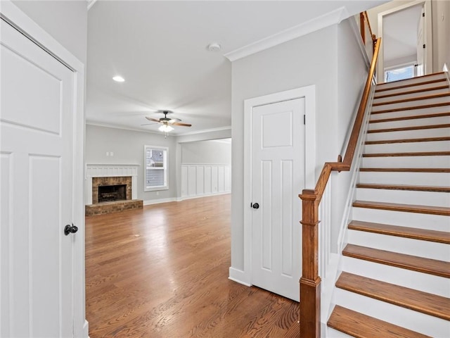 unfurnished living room with hardwood / wood-style flooring, crown molding, a brick fireplace, and ceiling fan