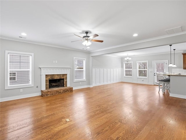 unfurnished living room featuring crown molding, a fireplace, ceiling fan with notable chandelier, and light hardwood / wood-style flooring