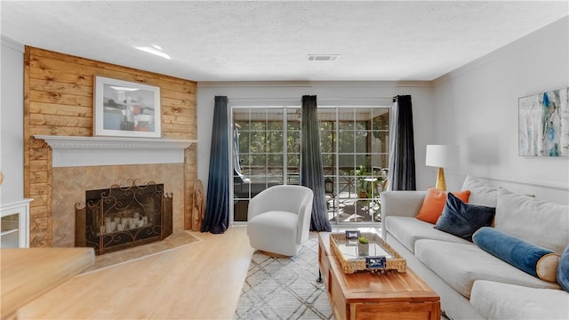 living room featuring a tile fireplace, crown molding, a textured ceiling, wooden walls, and light wood-type flooring