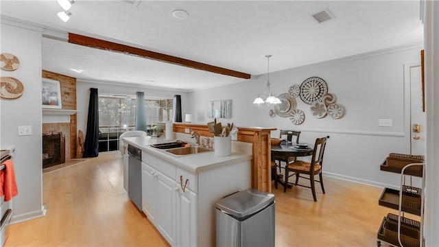 kitchen with sink, stainless steel dishwasher, pendant lighting, a tiled fireplace, and white cabinets