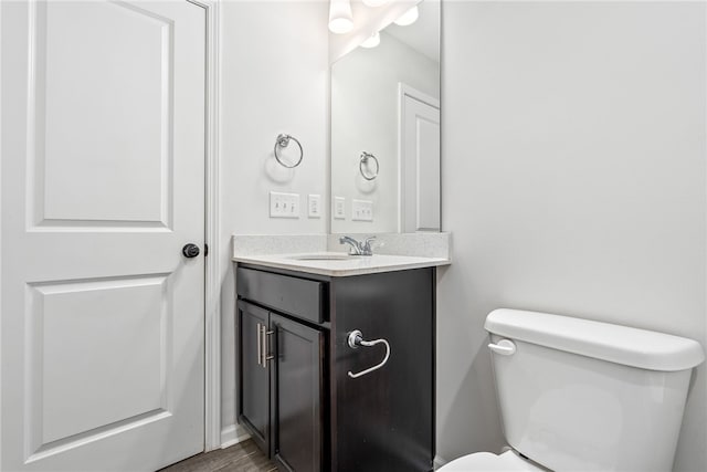 half bathroom with toilet, wood finished floors, and vanity