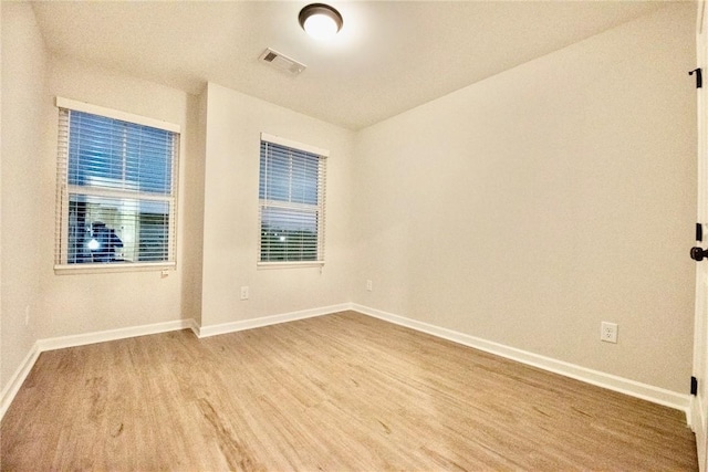 empty room featuring visible vents, wood finished floors, and baseboards