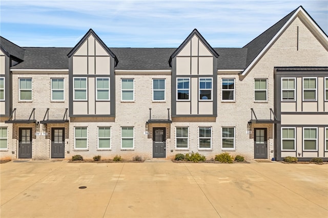 townhome / multi-family property with a shingled roof and brick siding