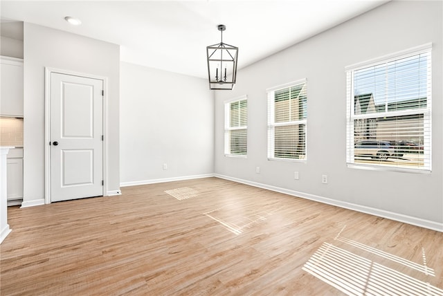 empty room with a chandelier, baseboards, and light wood-style flooring