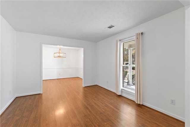 empty room featuring hardwood / wood-style flooring and a notable chandelier