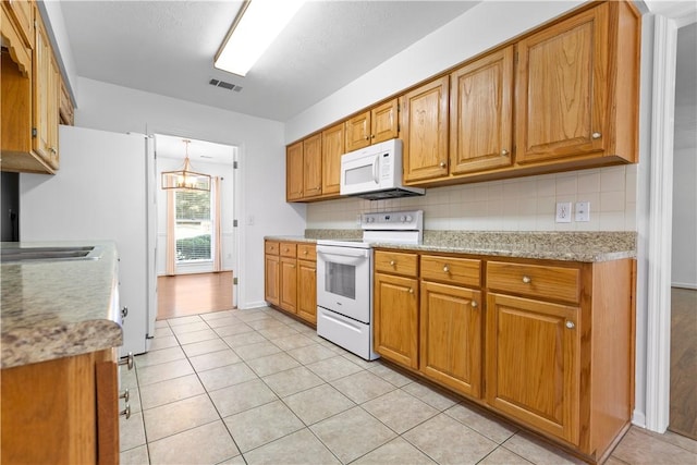 kitchen featuring white appliances, backsplash, light stone countertops, light tile patterned floors, and a notable chandelier