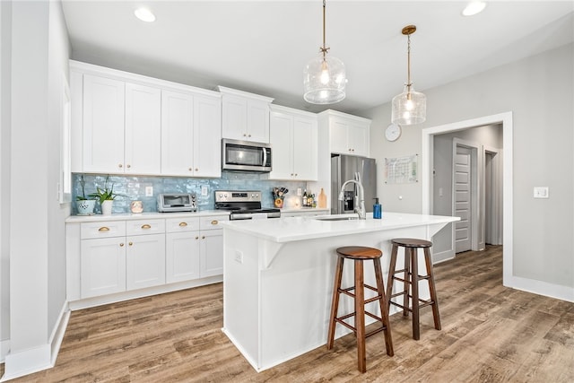 1242 Burrow Cir, Opelika, AL 36801 - kitchen featuring appliances with stainless steel finishes, decorative backsplash, an island with sink, light countertops, and light wood-style floors