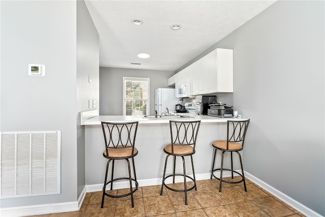 kitchen with white appliances, a breakfast bar, white cabinets, and a peninsula