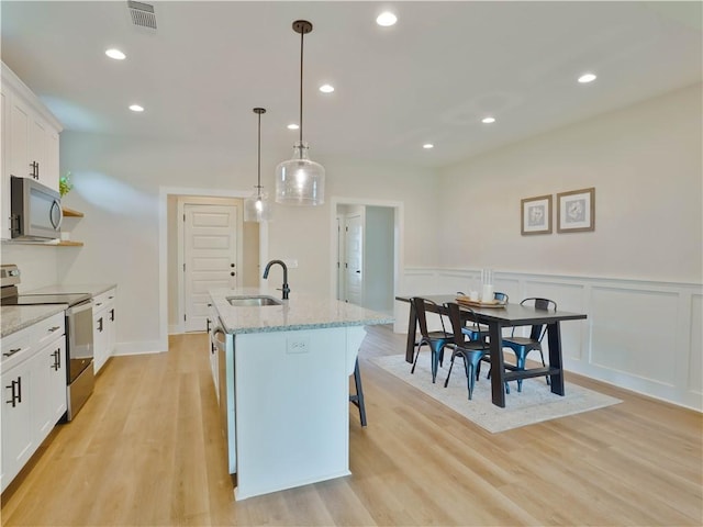 1003 Crossing Ct E, Valley, AL 36854 - kitchen featuring appliances with stainless steel finishes, a kitchen island with sink, white cabinets, a wainscoted wall, and light wood-type flooring