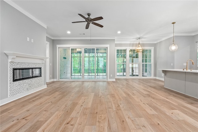 unfurnished living room with crown molding, ceiling fan, light wood-type flooring, a sink, and a tile fireplace