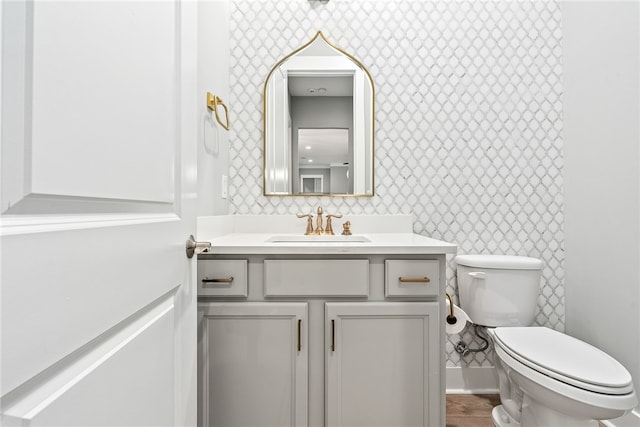 bathroom featuring toilet, wallpapered walls, and vanity