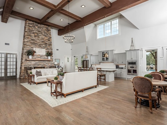living area featuring beamed ceiling, visible vents, a high ceiling, wood finished floors, and a notable chandelier