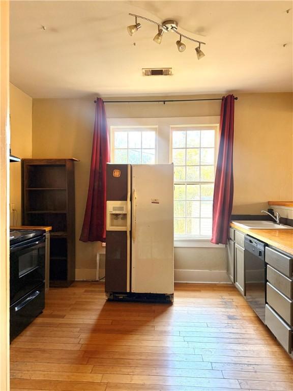 kitchen featuring light wood-type flooring, sink, dishwasher, black electric range oven, and white fridge with ice dispenser