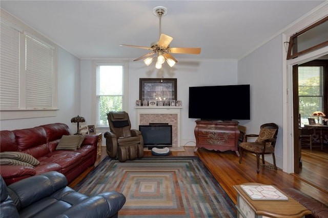 living room with a fireplace with flush hearth, a ceiling fan, wood finished floors, and crown molding