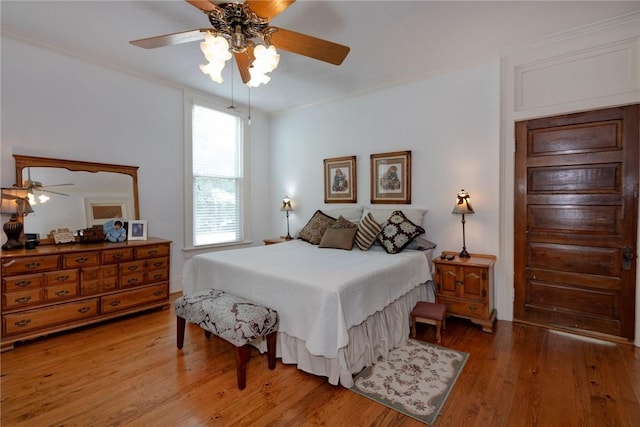 bedroom featuring crown molding, light wood-style flooring, and a ceiling fan