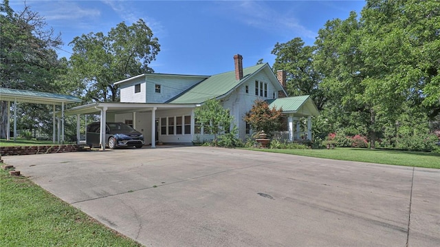 view of front facade with an attached carport, concrete driveway, a front yard, and metal roof