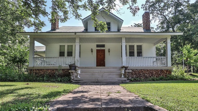 view of front of home with covered porch, a chimney, a front yard, and metal roof