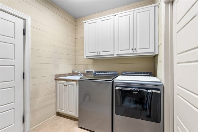 clothes washing area with sink, cabinets, light tile patterned floors, wooden walls, and washer and clothes dryer