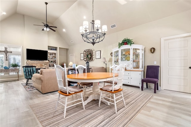 dining space with light hardwood / wood-style flooring, built in features, high vaulted ceiling, a fireplace, and ceiling fan with notable chandelier