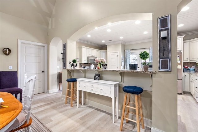 kitchen with light wood-type flooring, appliances with stainless steel finishes, a kitchen breakfast bar, light stone countertops, and white cabinets