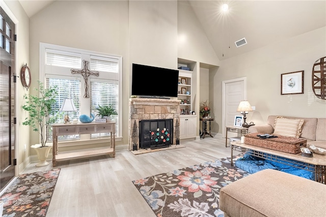 living room featuring a stone fireplace, built in features, high vaulted ceiling, and light wood-type flooring