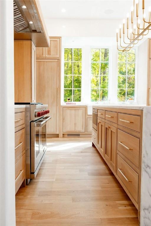 interior space featuring light brown cabinets, a notable chandelier, high end stove, light hardwood / wood-style floors, and decorative light fixtures