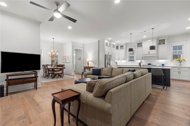 living room featuring ceiling fan with notable chandelier, light hardwood / wood-style floors, crown molding, and sink