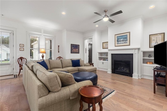 living room featuring ceiling fan, built in features, crown molding, and light hardwood / wood-style flooring