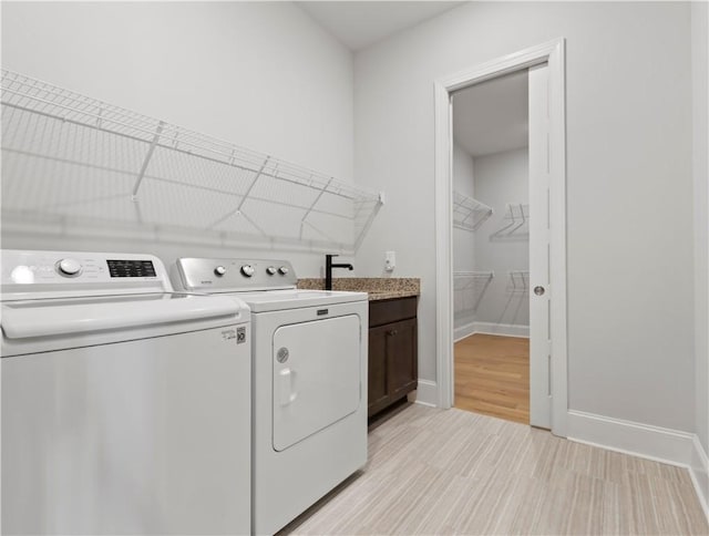 laundry room featuring cabinet space, baseboards, light wood-style flooring, independent washer and dryer, and a sink