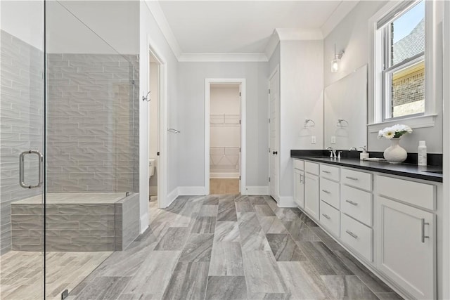 bathroom with vanity, baseboards, a spacious closet, a stall shower, and crown molding