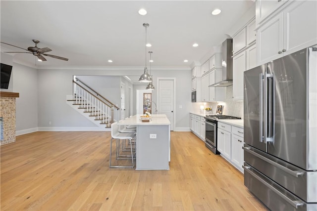 kitchen featuring a kitchen island with sink, stainless steel appliances, light countertops, ornamental molding, and wall chimney range hood