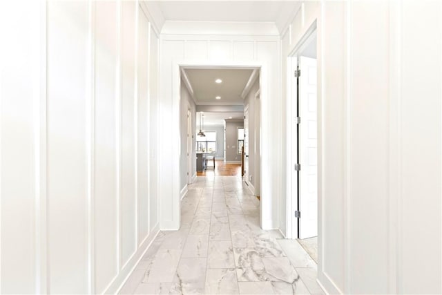 corridor with ornamental molding, marble finish floor, a decorative wall, and baseboards