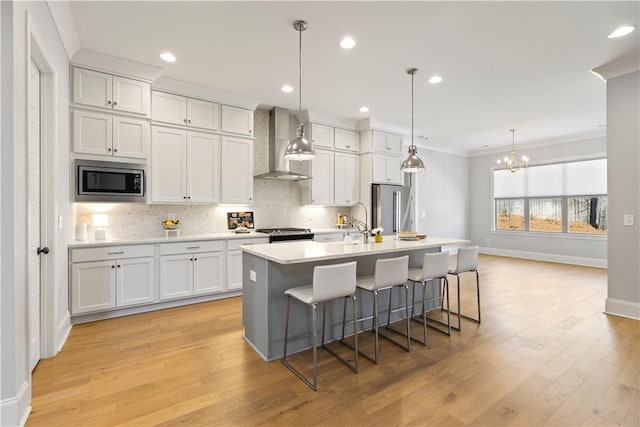 kitchen with tasteful backsplash, appliances with stainless steel finishes, ornamental molding, an island with sink, and wall chimney exhaust hood