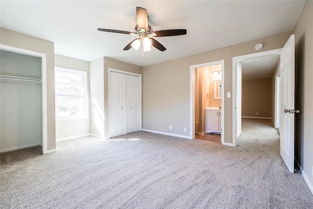 unfurnished bedroom with light carpet, connected bathroom, ceiling fan, and multiple closets