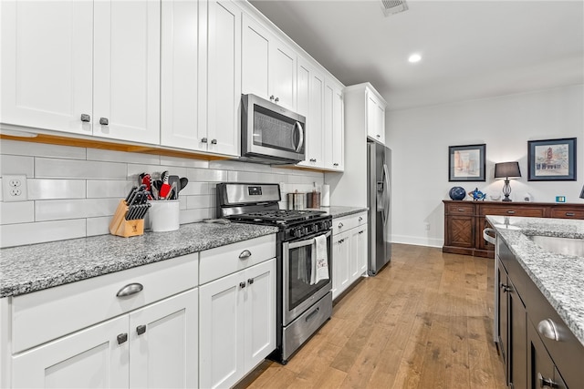 kitchen with white cabinetry, tasteful backsplash, light stone counters, light hardwood / wood-style flooring, and appliances with stainless steel finishes