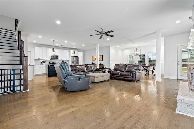 living room with ceiling fan with notable chandelier, light hardwood / wood-style floors, and decorative columns