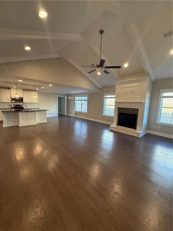 unfurnished living room featuring dark hardwood / wood-style flooring, vaulted ceiling with beams, ceiling fan, and a healthy amount of sunlight