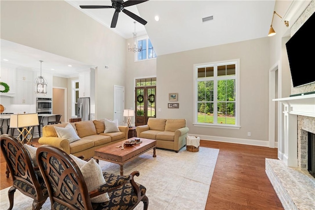 living room featuring a high ceiling, wood-type flooring, ceiling fan with notable chandelier, and crown molding