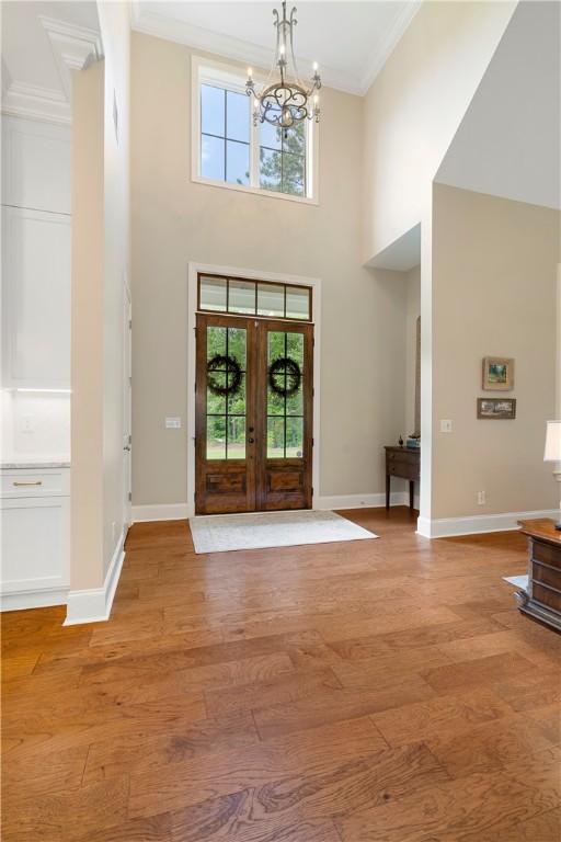 foyer entrance featuring french doors, baseboards, crown molding, and light wood finished floors